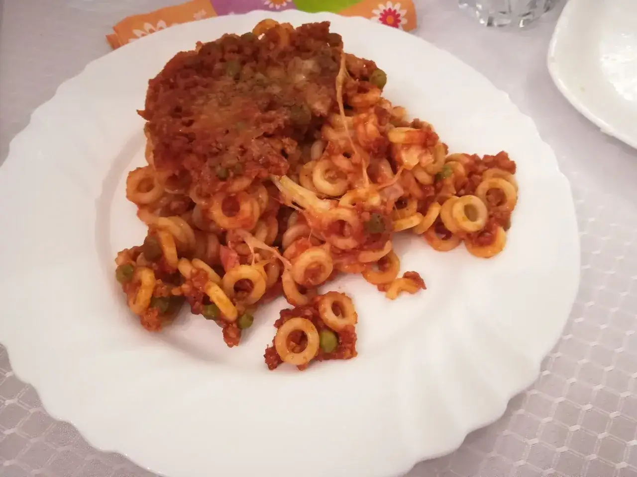 Piatto di anelletti al forno con ragù, piselli e formaggio filante. Un classico della cucina siciliana, pronto per essere gustato.