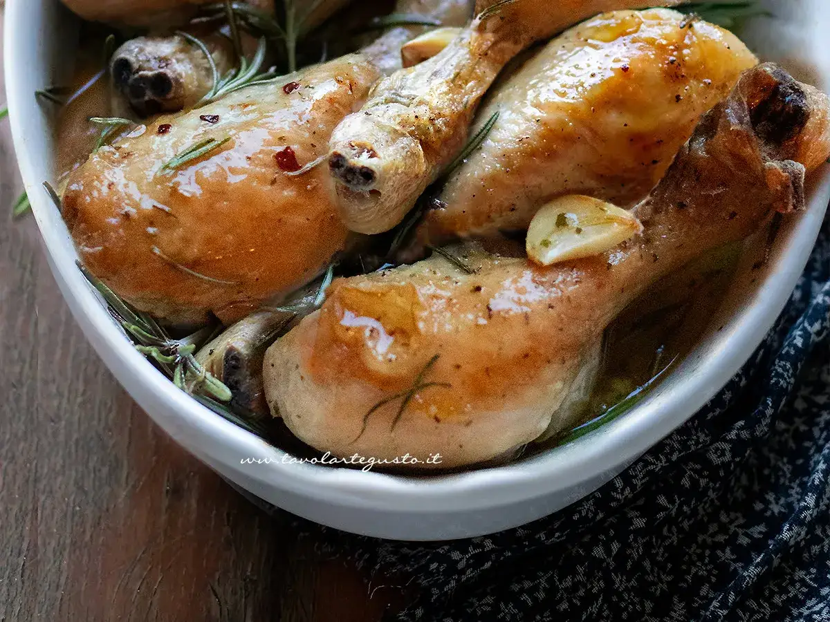 Cosce di pollo succulente in una teglia bianca, condite con aglio e rosmarino. Un'idea per gustose ricette di cosce di pollo.