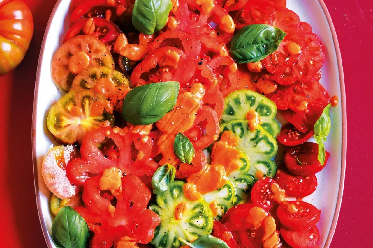 Un colorato carpaccio di pomodoro, con fette rosse e verdi condite con basilico fresco e pepe.