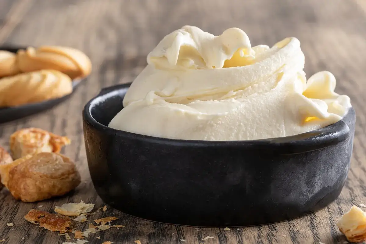 Un cremoso gelato fatto in casa, servito in una ciotola nera, con biscotti e sfoglie croccanti su un tavolo di legno.