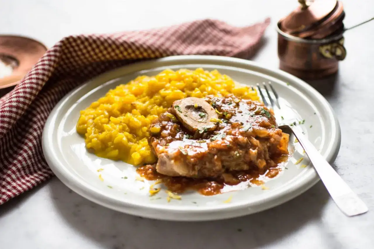 Un saporito ossobuco alla milanese con risotto giallo, guarnito con prezzemolo e scorza di limone.
