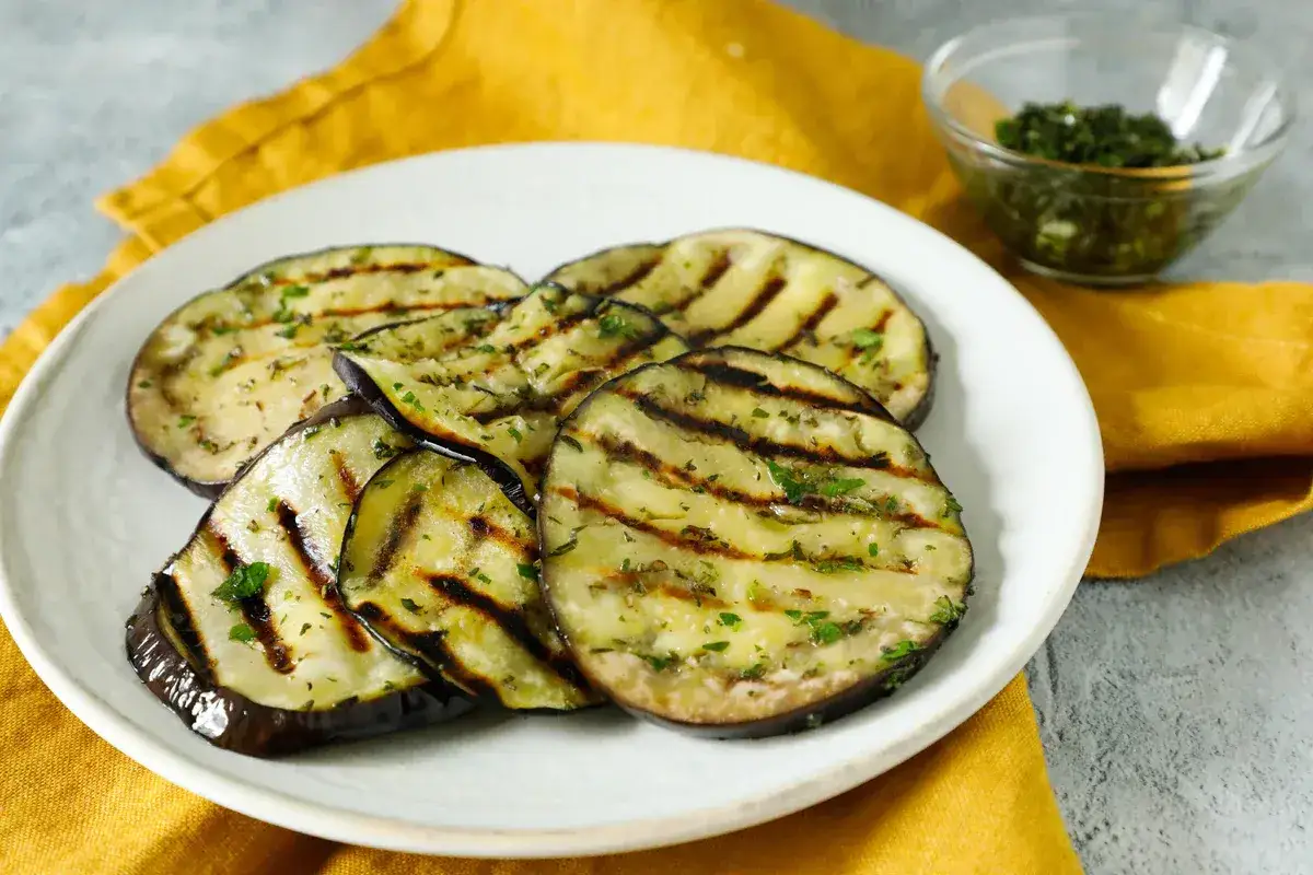 Melanzane grigliate condite con erbe aromatiche, pronte per essere gustate. Un'idea semplice su come condire le verdure grigliate per un contorno saporito.