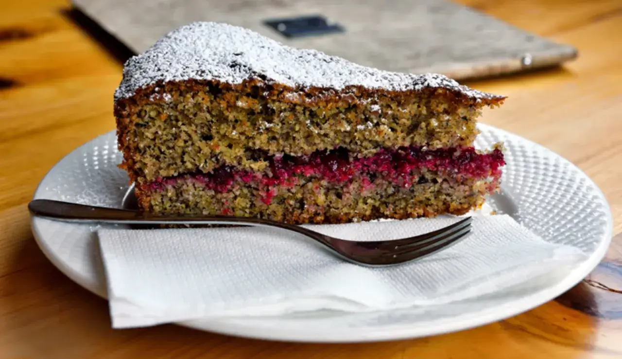 Una fetta di torta grano saraceno soffice, con ripieno di marmellata di frutti rossi, spolverata di zucchero a velo.