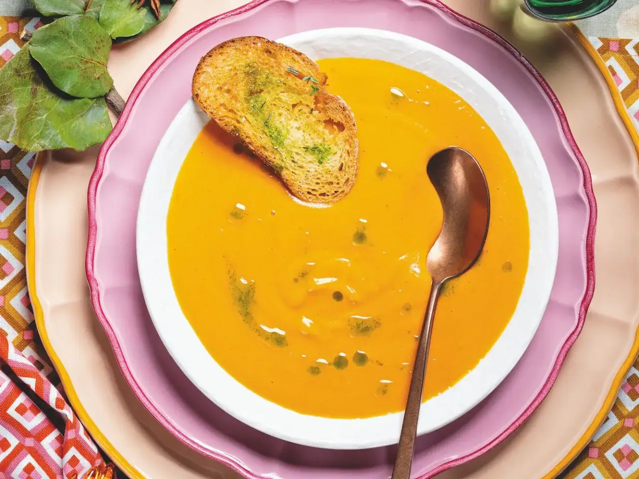 Zuppa cremosa di patate dolci, perfetta per le tue ricette autunnali. Servita con crostino aromatico e cucchiaio di rame.