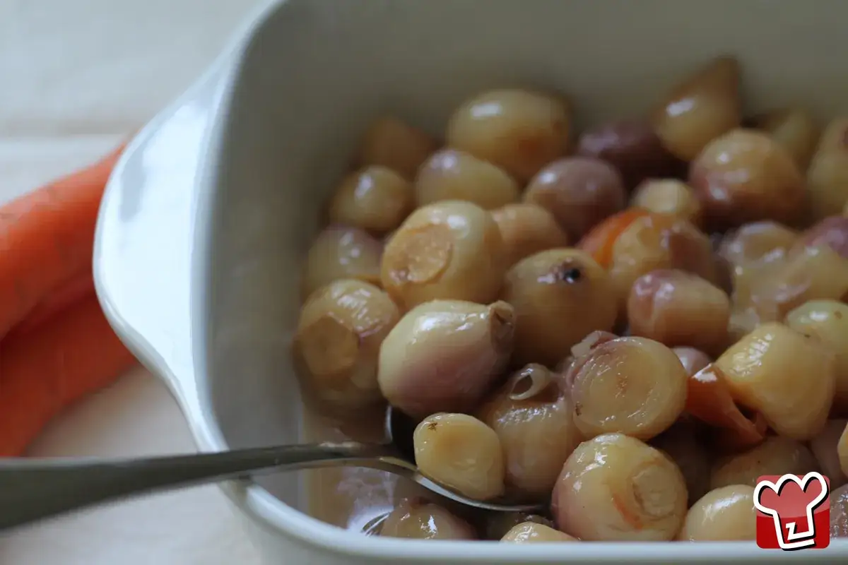 Lampascioni, cipolline dolci e saporite, in una ciotola bianca con una carota sullo sfondo.