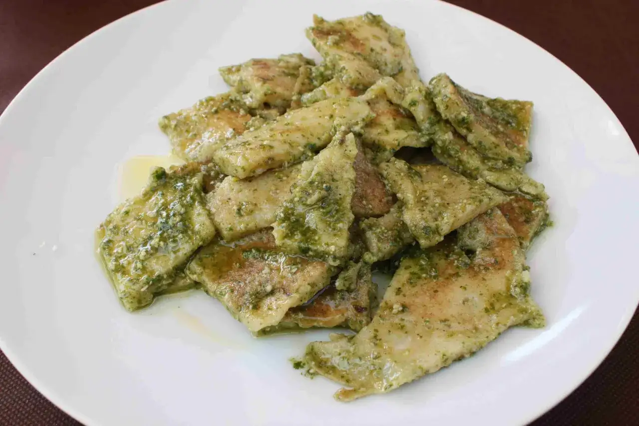 Piatto di testaroli al pesto, pasta tipica ligure condita con un sugo verde brillante a base di basilico, pinoli, aglio, parmigiano e olio d'oliva.