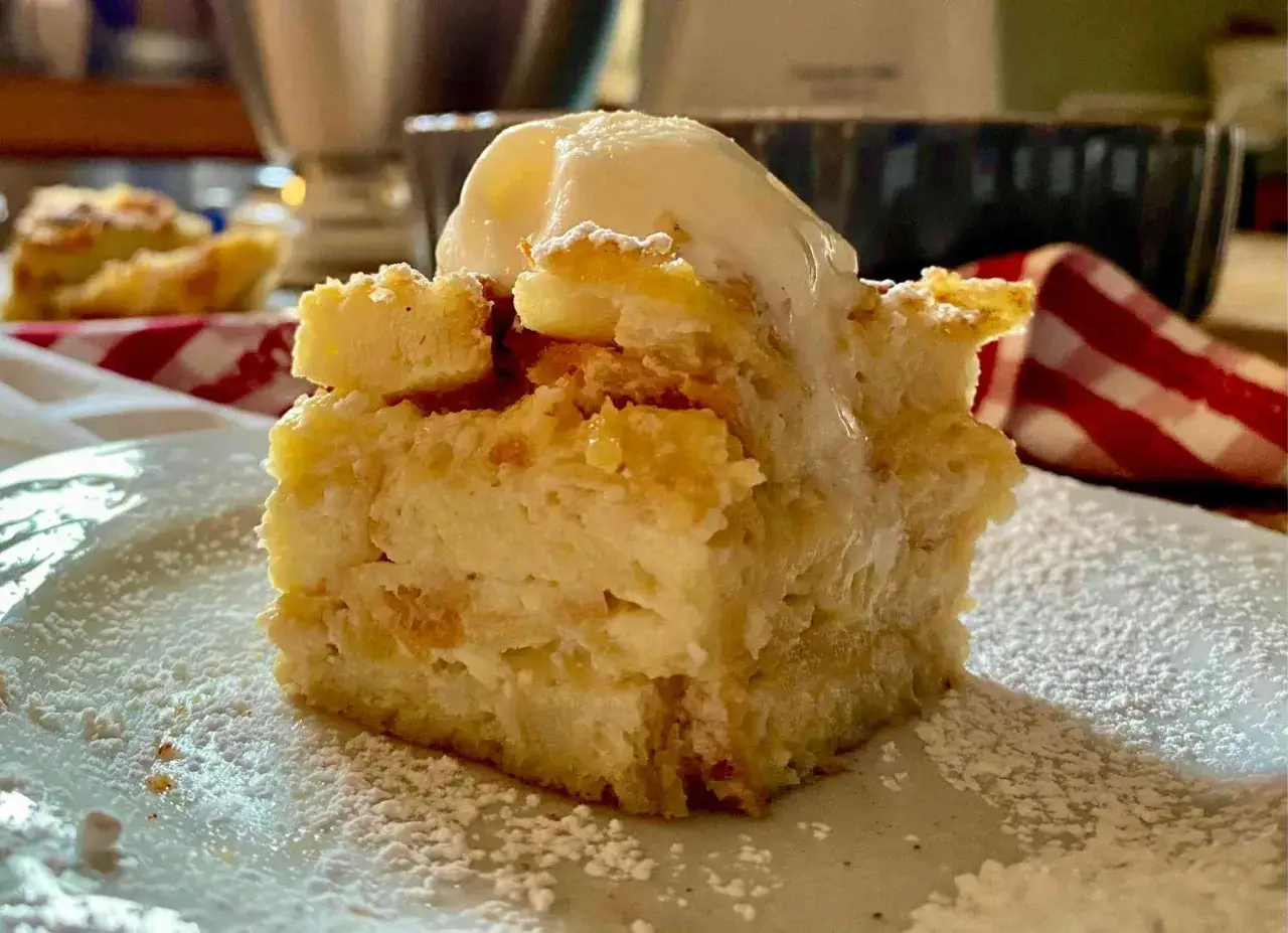 Una fetta di torta di pane raffermo mele e uvetta, cosparsa di zucchero a velo e sormontata da una pallina di gelato.