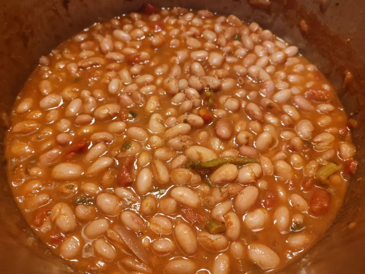 Un primo piano di fagioli in umido, ricchi e saporiti, cotti lentamente in un sugo di pomodoro e verdure.