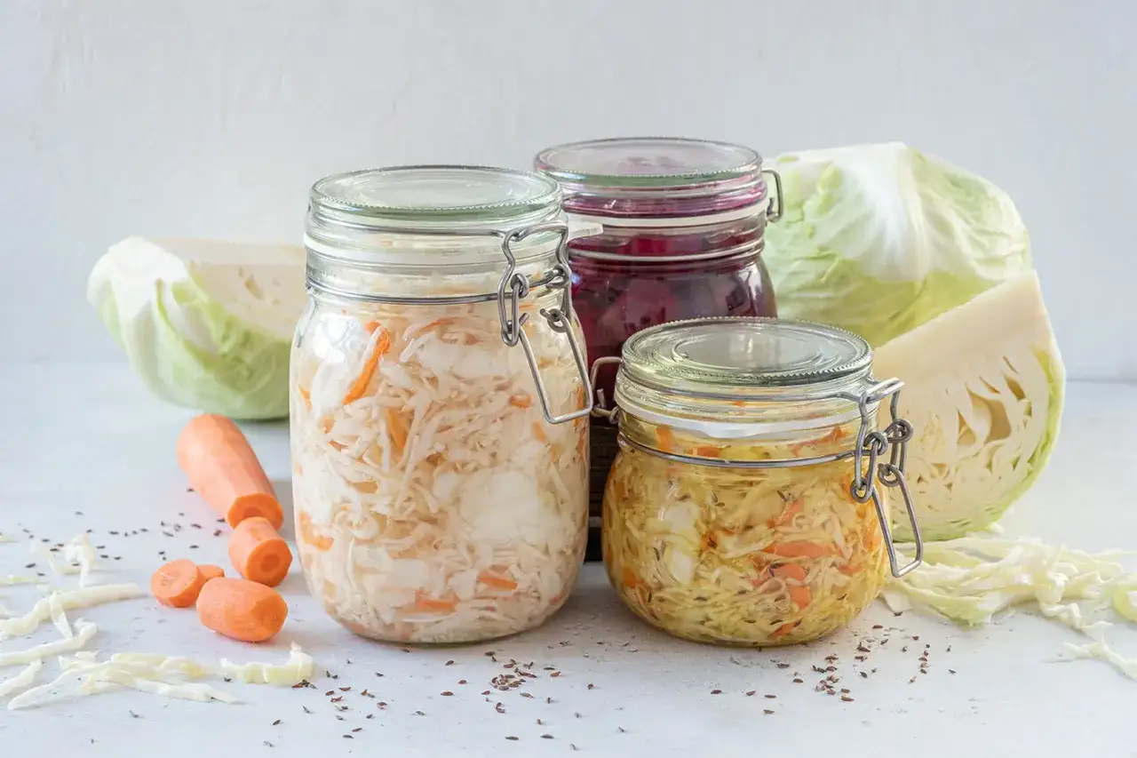 Barattoli di cibi fermentati fatti in casa: crauti, cavolo rosso e carote. Ingredienti freschi e semi di cumino sparsi.
