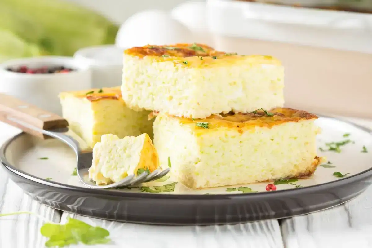 Una deliziosa frittata al forno soffice e alta, tagliata a cubetti e servita su un piatto, con un pezzetto su una forchetta.