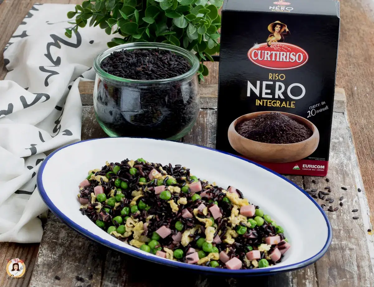 Piatto di riso nero integrale con piselli e prosciutto cotto, pronto per la cottura. Accanto, un barattolo di riso nero e la confezione Curtiriso.