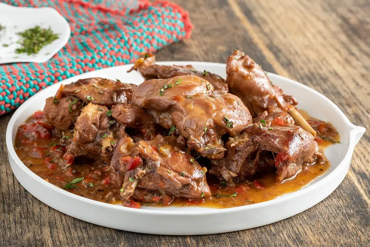 Piatto di coniglio in umido con peperoni rossi e verdi, guarnito con erbe aromatiche.