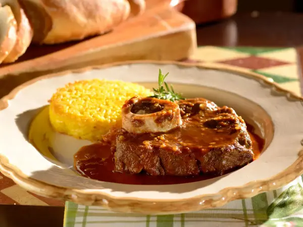 Un succulento ossobuco alla milanese, cotto lentamente e servito con polenta gialla e un rametto di rosmarino.