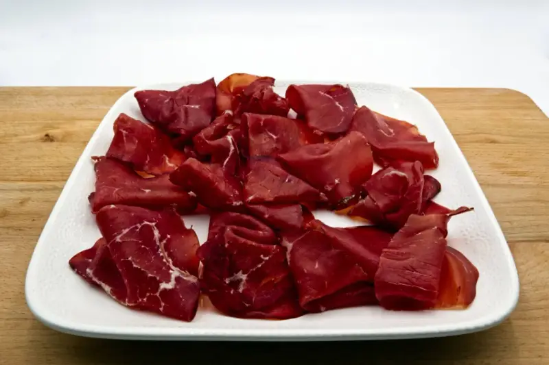 Fette di bresaola, la bresaola che carne è, su un piatto bianco.